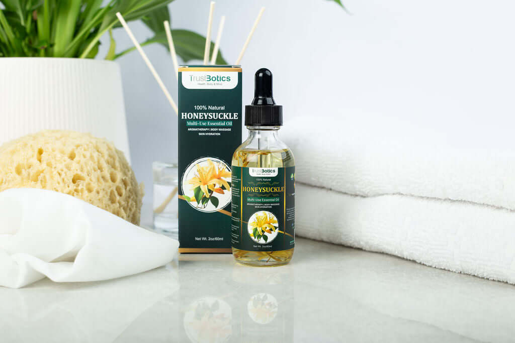Honeysuckle Essential Oil with packaging by TrustBotics displayed on spa-inspired white background, featuring towel, sponge, and diffuser.