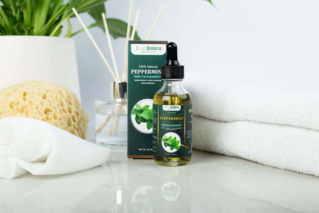 TrustBotics Peppermint Essential Oil bottle and box arranged with a bath sponge, white towel, and reed diffuser, evoking a luxurious and refreshing spa atmosphere.