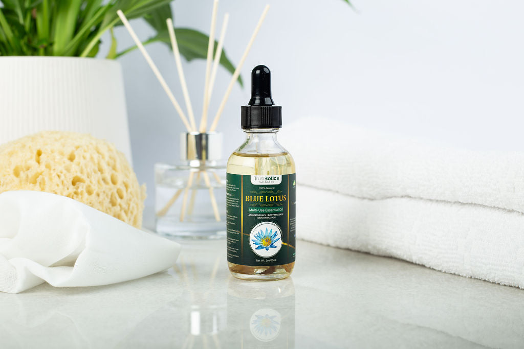 TrustBotics Blue Lotus Essential Oil bottle styled with spa accessories: towels, sponge, diffuser sticks, and green plant for a luxurious self-care vibe.