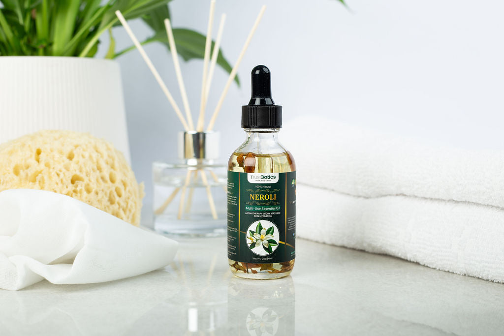 TrustBotics Neroli Multi-Use Essential Oil bottle styled on spa-inspired white surface with natural sponge, green plant, and diffuser sticks, highlighting luxurious self-care.