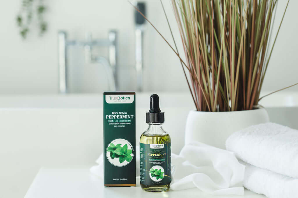 TrustBotics Peppermint Multi-Use Essential Oil bottle and box on a bathroom counter with plants and towels.