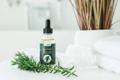 TrustBotics Rosemary Essential Oil bottle with fresh rosemary sprigs on a spa setting, highlighting natural skincare and wellness benefits.