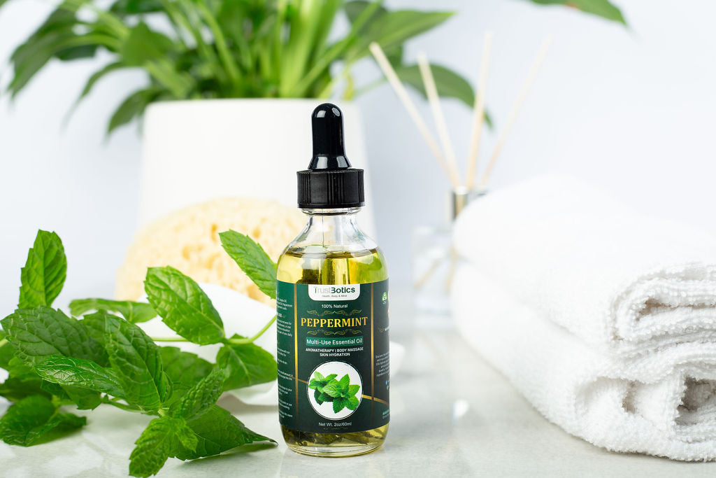 TrustBotics Peppermint Essential Oil bottle surrounded by fresh mint leaves, with a spa towel and green plant in the background, symbolizing natural freshness and rejuvenation.